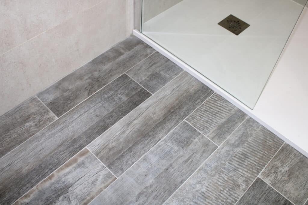 Carrelage imitation bois gris, receveur de douche moderne Carrelage imitation bois gris posé en diagonale devant un receveur de douche blanc avec grille d'évacuation carrée.